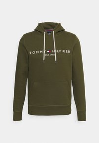 Sudadera color oliva con cordones blancos, bolsillo frontal y el logo "Tommy Hilfiger Est. 1985" en el pecho.