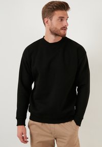Hanorac negru dintr-un amestec de bumbac, cu gât rotund, mâneci lungi, manșete ribbate și o croială lejeră.