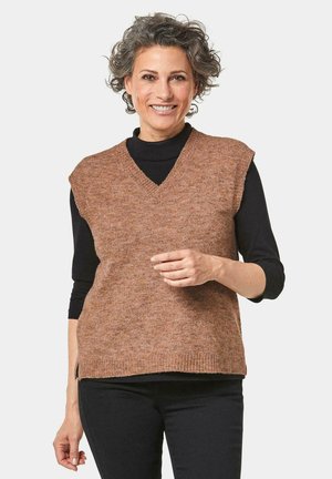 Brauner gestrickter Pullunder mit V-Ausschnitt und kurzen Ärmeln, getragen über einem schwarzen Langarmtop. Der Stoff hat eine weiche Textur und ein dezentes Muster.