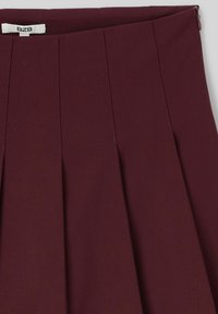 Jupe plissée bordeaux avec une texture lisse, présentant quatre plis verticaux et une fermeture éclair sur le côté. Étiquetée avec une étiquette "BZB" à l'intérieur.