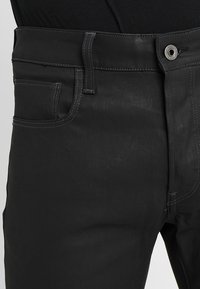 Svarta denimjeans med en åtsittande design. Funktioner inkluderar en framficka, bältesslingor och en metallknäppning. Diskret texturerad yta.