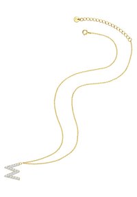 Guldhalsband med en stiliserad "M"-berlock prydd med klara ädelstenar. Kedjan har ett spänne och en justerbar längd.