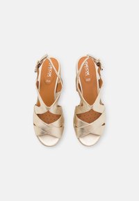 Paire de sandales métalliques dorées à bout ouvert avec brides croisées, boucle à la cheville et semelles intérieures perforées marron, vues de dessus sur fond blanc.