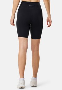 Shorts neri da ciclismo con vita alta, realizzati in tessuto liscio e elasticizzato. Presentano un logo discreto sul retro e arrivano a metà coscia.