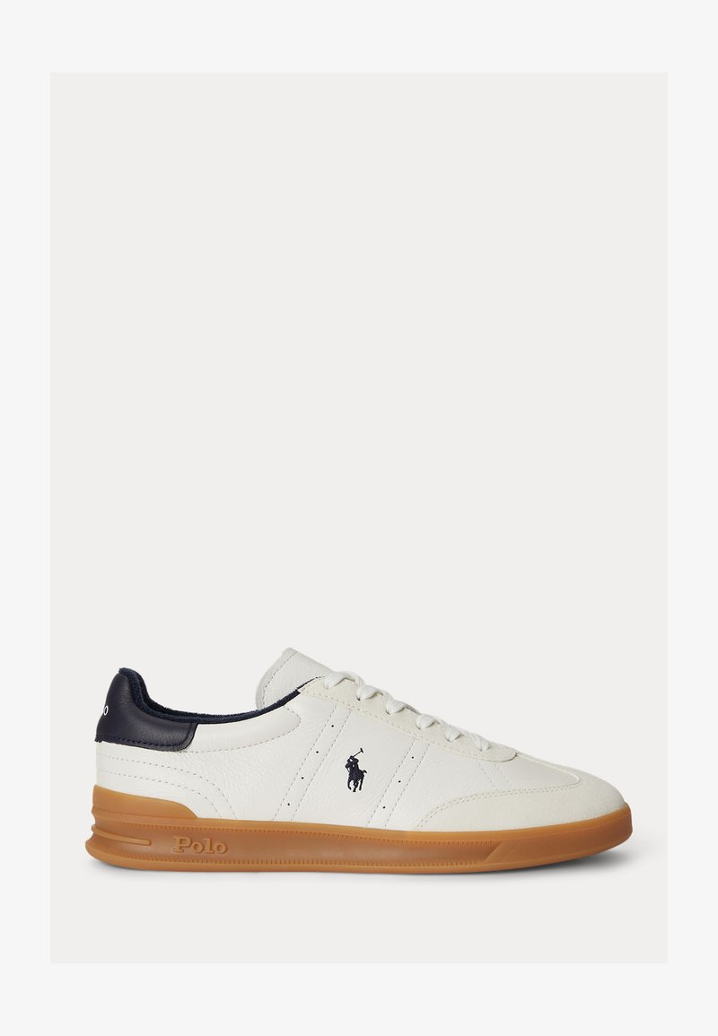 Hvit lær lavtopp sneaker med marineblå hælflik, snøring foran, såle av gummirubber og svart Polo-logo på siden.