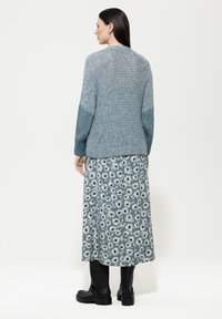 Hellblaues gestricktes Sweatshirt mit strukturiertem Stoff, kombiniert mit einem langen Rock mit Blumenmuster, der Gänseblümchen auf einem dunkelblauen Hintergrund zeigt. Schwarze Knöchelstiefel.