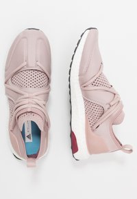 Des chaussures de sport rose clair dotées d'un dessus en maille, d'un système de laçage élastique et d'une semelle en caoutchouc texturée avec un intercalaire blanc et des accents rouges.