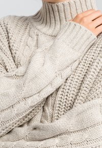 Kermaankelpoinen neulepaita, jossa korkea resorikaulus ja palmikkoneulekuviot, erilaisilla tekstuureilla kankaan eri osissa.