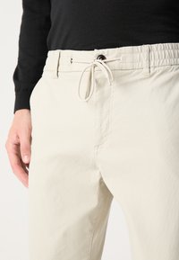 Pantalones beige de cintura elástica con cordón, con bolsillos frontales y una tela suave y ligera con una sutil textura.