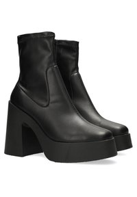Botines negros de cuero liso, con un tacón grueso y suela de plataforma, con un diseño elegante y minimalista y cierre lateral con cremallera.