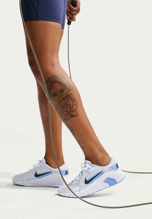 Personne portant des baskets Nike blanches et bleues et un short bleu marine saute à la corde, montrant un tatouage détaillé d'une femme et d'une fleur sur sa jambe.