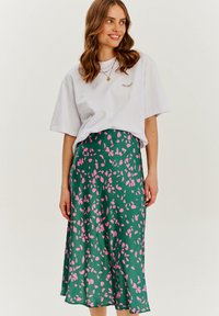Zielona spódnica z różowym wzorem liści, wykonana z miękkiego materiału. W połączeniu z białą koszulką z kolorowym haftem rzęs.