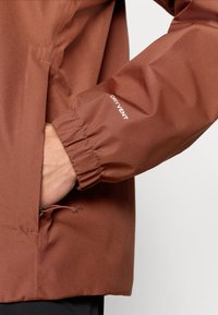 Καφέ αδιάβροχο μπουφάν με ελαστικές μανσέτες, που διαθέτει χέρι σε τσέπη και το λογότυπο "DRY VENT" στο μαν ίκι. Ομαλή, ανθεκτική υφή υφάσματος.