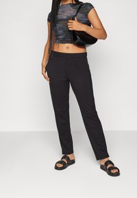 Černé kalhoty na míru s úzkým střihem, s hladkým povrchem, poutky na opasek a bočními kapsami. Pár s krátkým texturovaným topem a černými sandály.