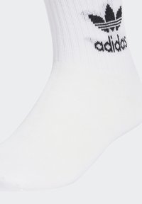Fehér crew zokni bordás mintával, fekete Adidas logóval és a felső részen, a szélén elhelyezett háromlevelű dizájnnal.