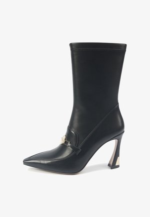 Black leather ankle boot with a pointed toe, high heel, and decorative gold hardware strap. Smooth texture and fitted design.