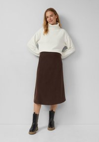 Witte, knusse coltrui gecombineerd met een bruine rok tot op de knie. Zwarte enkellaarsjes met bruine zolen. Eenvoudig, strak ontwerp in neutrale kleuren.