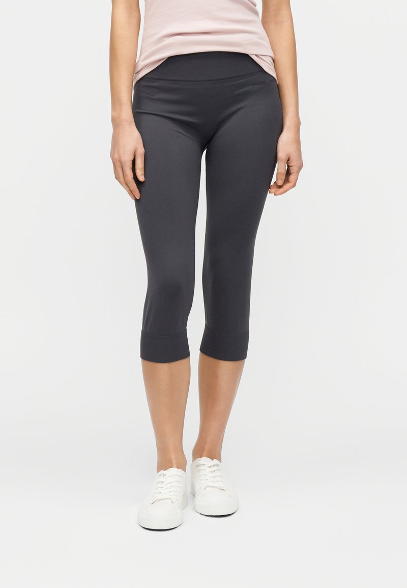 Leggings courts gris foncé en tissu extensible avec une large ceinture et une coupe ajustée. Des baskets blanches complètent la tenue.