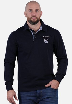 Polo à manches longues navy avec col, présentant un motif à carreaux sous le col et un logo brodé sur la poitrine.