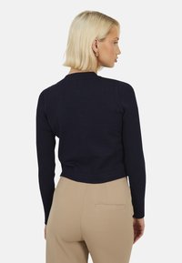 Marineblauwe cropped trui met ribgebreide mouwen, ronde halslijn en een gladde textuur, gecombineerd met beige broek met een achterzak.