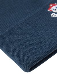 Berretto di lana blu con tessuto testurizzato. Presenta una piccola toppa con un personaggio ricamato sulla parte anteriore, posizionata di lato.