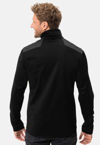Schwarze Fleecejacke mit hohem Kragen und kontrastierenden schwarzen Schulterpaneelen; hat lange Ärmel und eine glatte Textur.