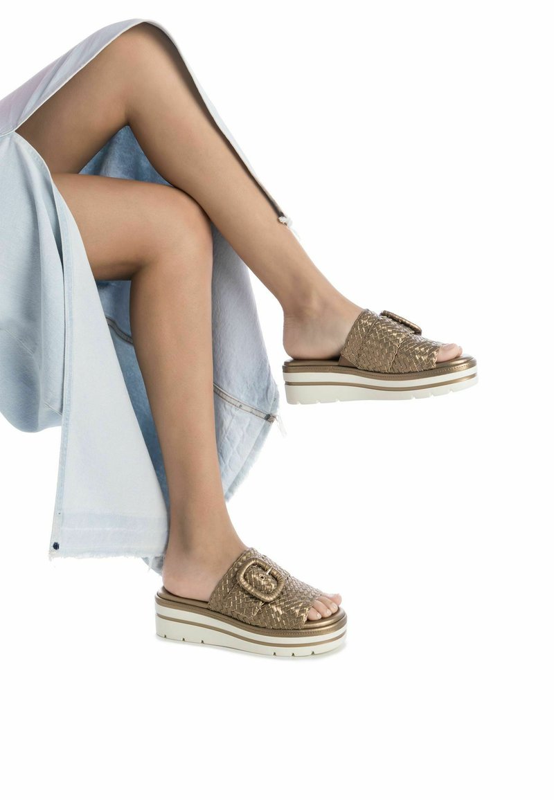 Chanclas de slide de hilo dorado con una suela blanca gruesa y un acento decorativo de hebilla. La parte superior presenta un diseño de patrón.