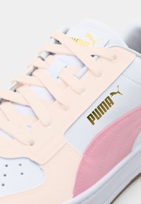 Hvide sneakers med bløde lyserøde accenter, tekstureret sål og guld "PUMA" logo. Har let lyserøde overlays og hvide snørebånd.