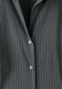 Tissu gris foncé à fines rayures avec deux boutons blancs attachés sur une chemise ou un chemisier à col.