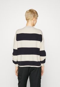 Pull en tricot avec des rayures crème et marine, présentant un col rond et une coupe ample. Le tissu semble doux avec des côtes aux poignets.