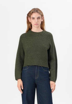 Suéter verde cropped con cuello y dobladillo acanalados, mangas largas y un patrón de punto texturizado, combinado con jeans oscuros de cintura alta.