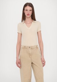Beige ribbed short-sleeve polo top with a V-neck and light tan baggy pants. The fabric is soft with visible stitching details.