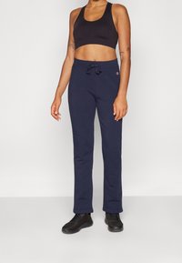 Mörkblå träningsoverallsbyxor med dragsko i midjan, kombinerat med en svart sport-bh. Båda är tillverkade av mjukt, elastiskt material som passar för aktivt användande.