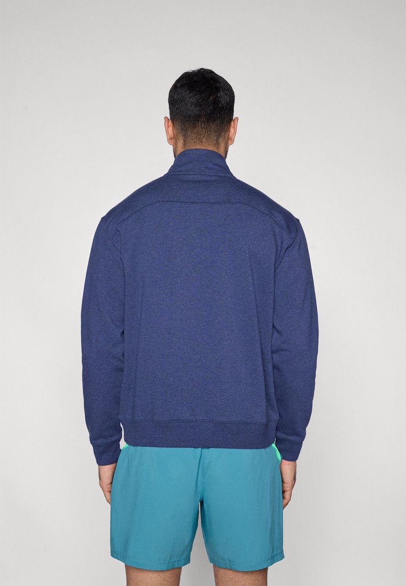 Sweat-shirt bleu marine avec col montant, tissu texturé, poignets et ourlet côtelés. Associé à un short aqua. Vue de dos.