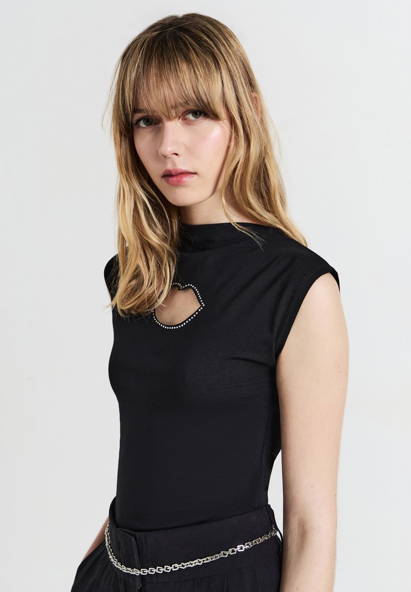 Top aderente nero con collo alto e un taglio decorativo accentuato da piccoli chiodi. Presenta maniche a carpa e una texture liscia.