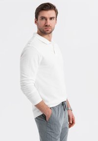 Vit långärmad polo-shirt med klassisk krage, bärs med grå randiga byxor. Har en avslappnad passform och mjukt material.