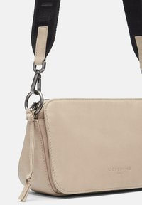 Beige Leder Umhängetasche mit glatter Oberfläche, ausgestattet mit einem abnehmbaren schwarzen geflochtenen Schulterriemen und silberfarbenen Beschlägen. Auffällige weiche Kanten.
