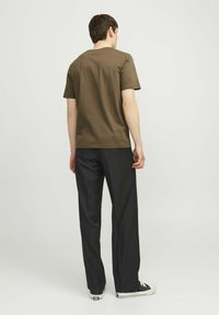 Olive green cotton t-shirt with short sleeves and a rounded neckline, paired with black trousers and black sneakers. Plain design, no patterns.