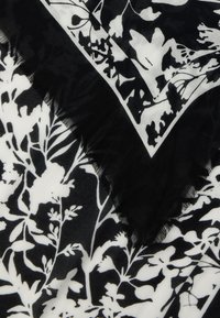 Svart og hvitt stoff med blomstermønster og sommerfugler, med et brettet hjørne og frynsete kanter.