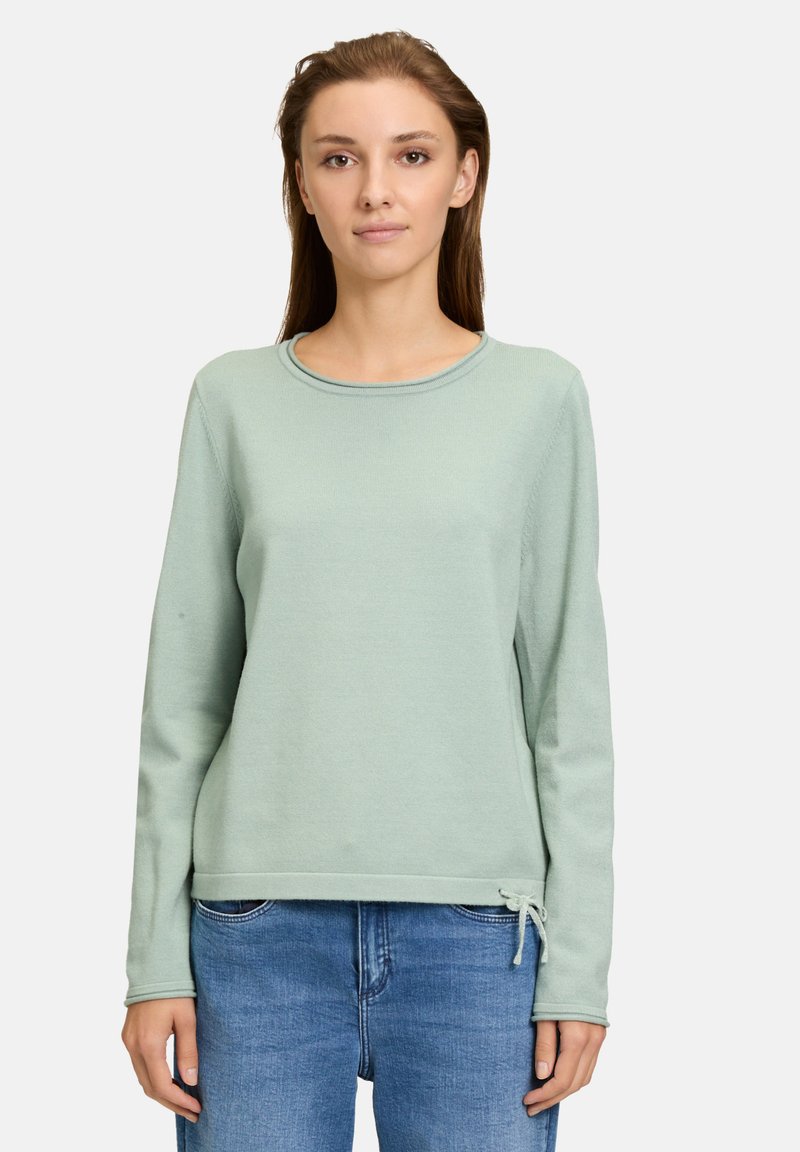 Mintgrüner Langarm-Sweatshirt mit Rundhalsausschnitt, strukturiertem Stoff und verstellbaren Bändern am Saum. Kombiniert mit blauen Jeans.