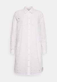 Camisa blanca de manga larga con cuello puntiagudo, adornada con intrincados patrones recortados y con botones en la parte frontal, fabricada en un tejido ligero.