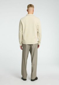 Polo de manga larga color beige claro con cuello, combinado con pantalones grises claros. Diseño sencillo y tejido texturizado.