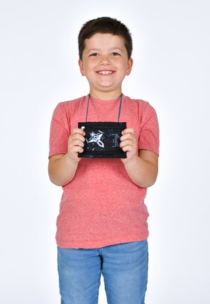 Schwarzer Stoffbeutel mit einem Weltraum-Design, das eine weiße Flugzeuggrafik und blaue Akzente aufweist, gehalten von einem Kind in einem roten Shirt und blauen Jeans.