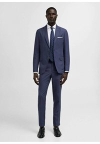 Marinblå jakkesæt lavet af et glat stof, der har en blazer med to knapper og slim-fit bukser. Accentueret med en hvid skjorte og en polka dot slipse.