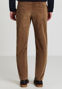 Braune Cordhosen mit weicher Textur, geradem Schnitt und Gesäßtaschen. Getragen mit schwarzen Schuhen mit dicker Sohle.