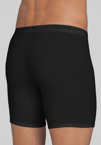 Boxer shorts Sloggi neri con una texture liscia, presentano una vita elastica nera con il logo del marchio, design aderente e lunghezza fino a metà coscia.