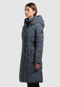 Dolga puhasta bunda s kapuco v temno sivi barvi. Ima vbodno zasnovo, sprednji zadrgo in elastične poudarke v predelu pasu.