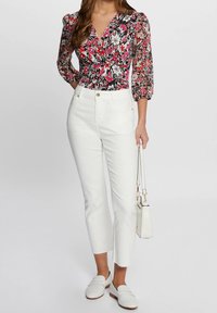 Blouse fleurie avec fond noir, fleurs roses et blanches ; associée à un jean blanc court. Accessoires compris : un petit sac à main blanc.