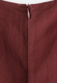 Gros plan d’un tissu bordeaux avec une fermeture éclair invisible partiellement fermée en haut au centre.