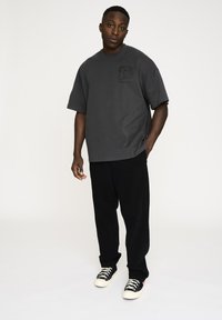 Grå oversized t-shirt med et grafisk print på brystet, parret med sorte brede bukser og sorte sneakers med hvide såler.